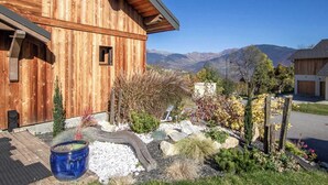 Un edificio in legno con tetto spiovente, immerso in un giardino curato con diverse piante e un vaso blu di grandi dimensioni.