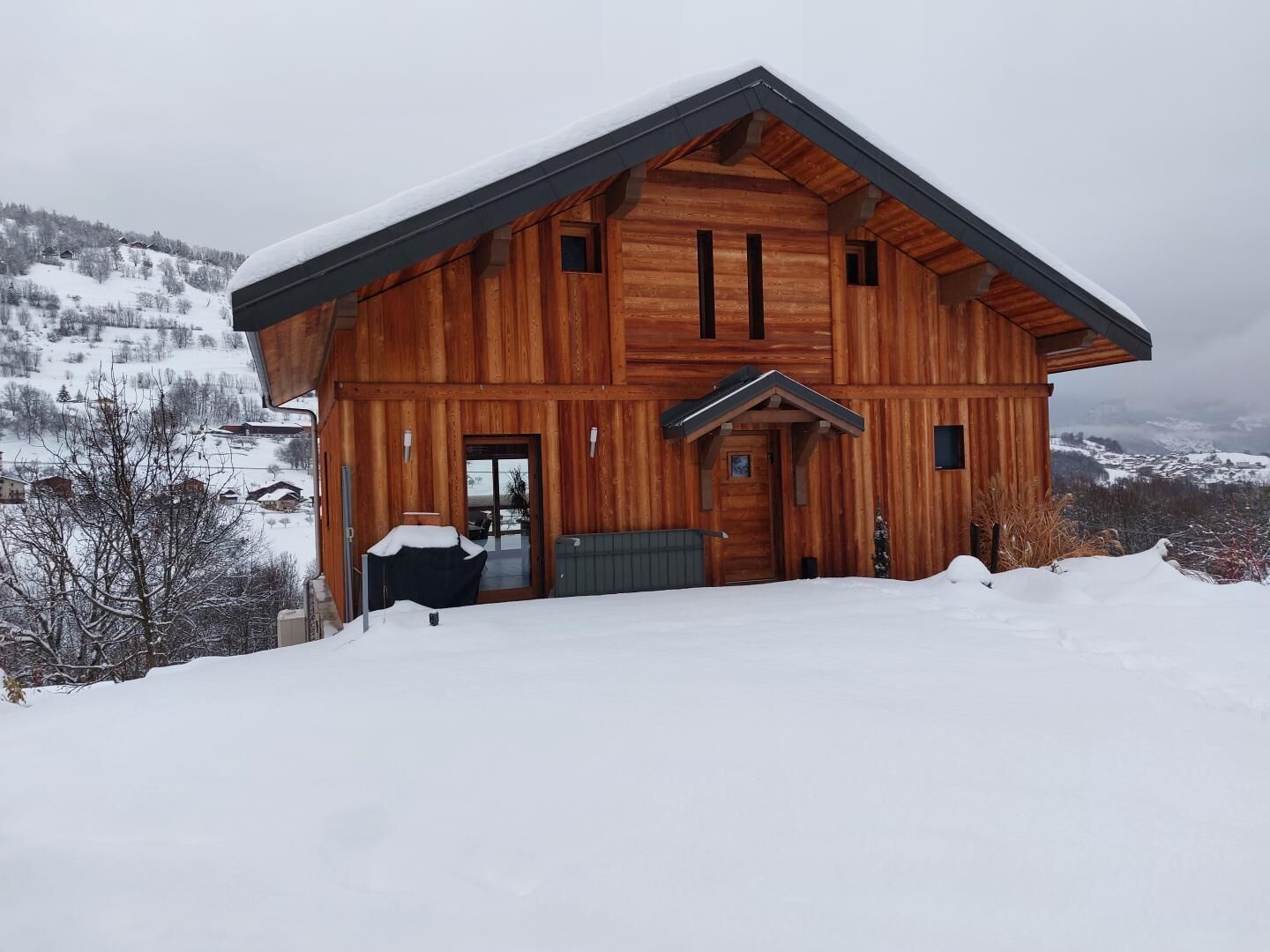 A wooden cabin with a sloped roof, a front entrance, and a view of snow-covered mountains.