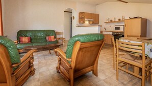 Een gezellige woonkamer met een groene leren bank, houten stoelen, een eettafel met een witte tafelkleed en een keuken met houten kastjes en apparatuur.