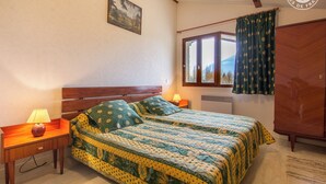 Een slaapkamer met een houten bed, twee nachtkastjes met lampen, een raam met gordijnen en een garderobe.