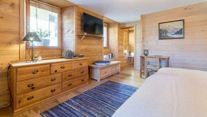 A wooden cabin bedroom with a bed, dresser, TV, and a painting on the wall. - Maison Adele - Ste-foy-tarentaise (SAINTE FOY TARENTAISE)