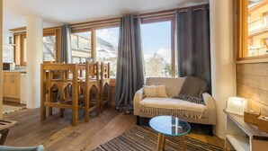 A cozy living room with a sofa, a glass coffee table, and a dining area with wooden chairs and a table. - Maison Adele - Ste-foy-tarentaise (SAINTE FOY TARENTAISE)