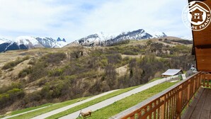 A wooden deck with a view of a mountain landscape, including a road and a cow. - LE Petit Bonheur - St-jean-d'arves (SAINT JEAN D'ARVES)