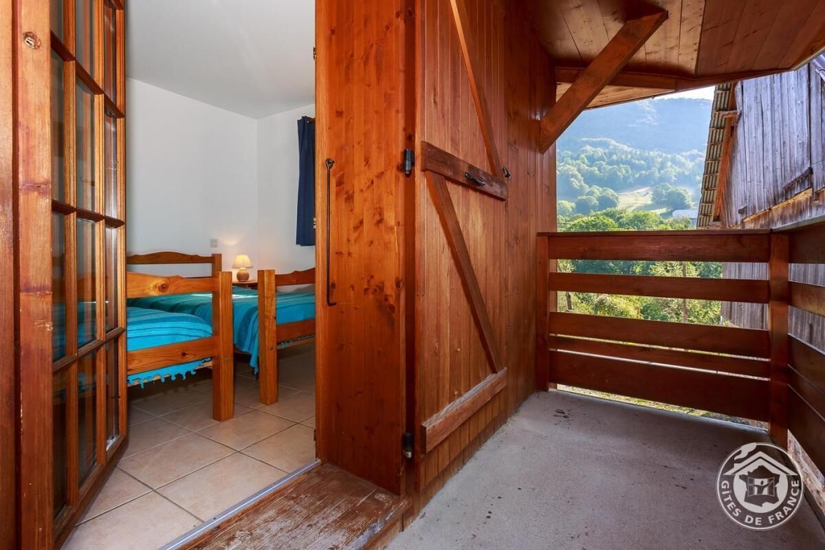 Una habitación de madera con una cama litera y un balcón con vistas a zonas verdes.