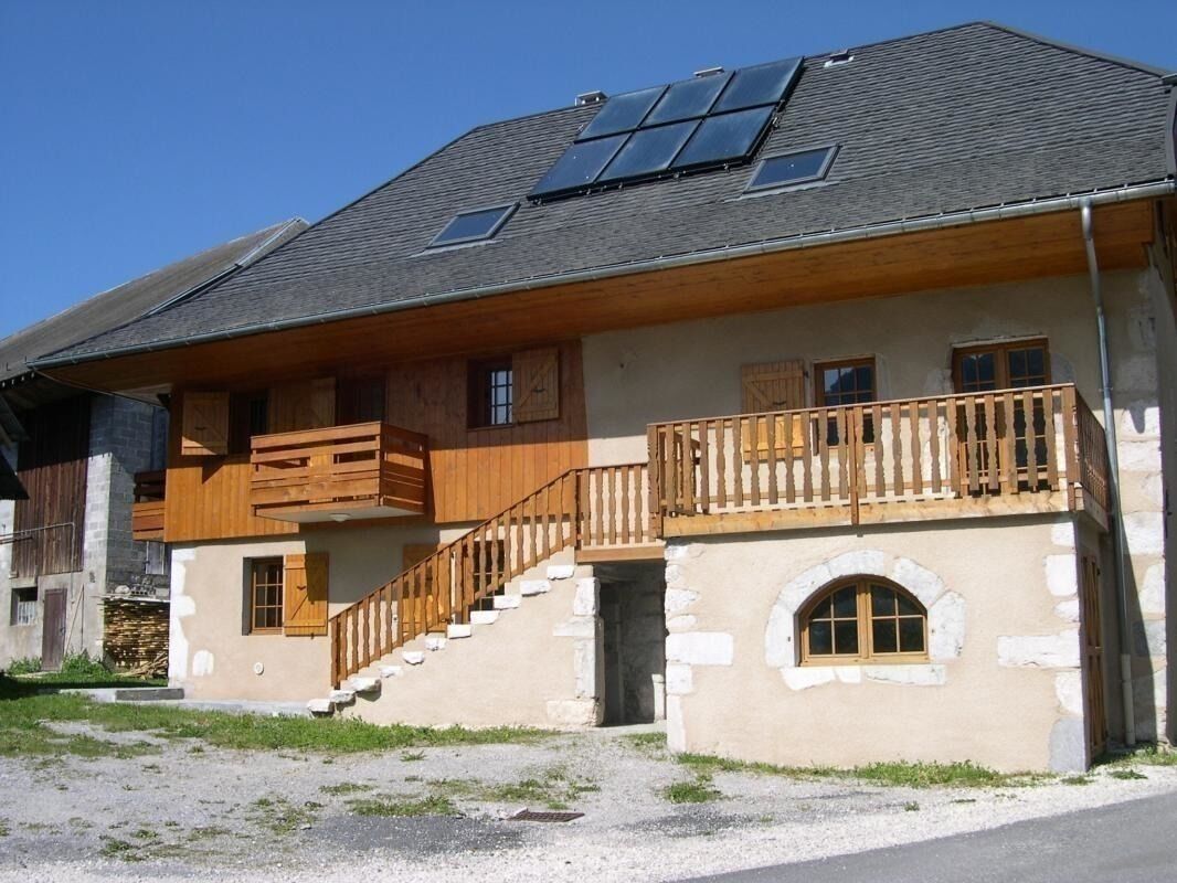 Een tweelaags huis met een houten balkon, een stenen fundering en zonnepanelen op het dak.