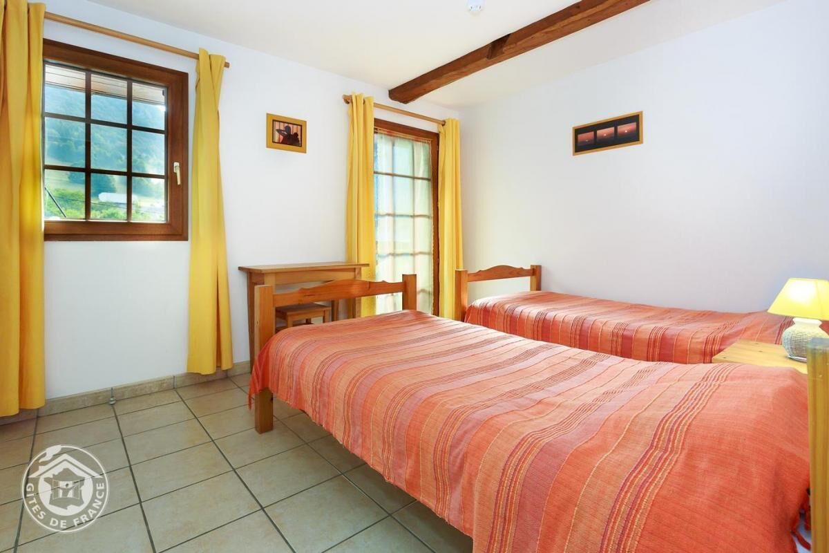 A room with two beds, a wooden desk, a window with curtains, and a small picture on the wall.