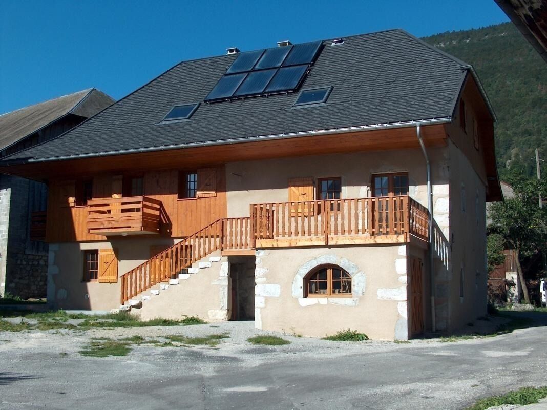 Un bâtiment à deux étages doté d’un balcon en bois, d’une entrée en pierre et de panneaux solaires sur le toit.