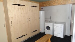 Een kleine wasruimte met twee wasmachines, een bankje en houten kasten.