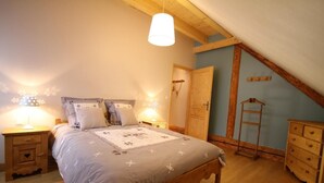 Een slaapkamer met een houten bed, twee nachtkastjes met lampen, een houten dressoir en een schuine plafond.
