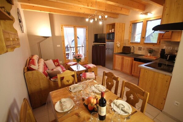 Un interno accogliente in legno, con un tavolo da pranzo apparecchiato, un angolo cottura dotato di elettrodomestici moderni e un soggiorno con divano e poltrone.
