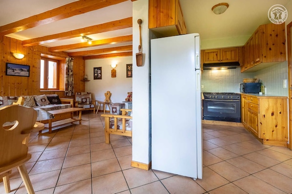 Tunnelmallinen, mökin tyylinen huone, jossa on puusisustus, ruokailutila penkeillä sekä keittiö, jossa on puukaapit ja liesi.