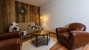 Un salon avec un mur en bois, un canapé, une table basse et des fauteuils en cuir.