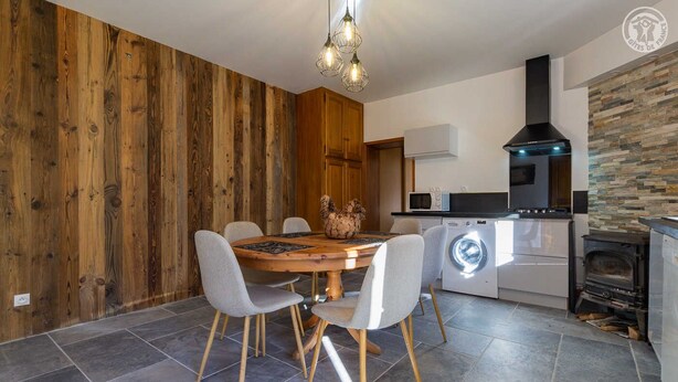 Une cuisine moderne avec un mur en bois, une table de salle à manger ronde entourée de chaises, un lave-linge et un poêle à bois.
