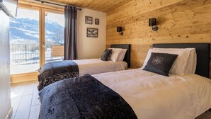 Une chambre avec deux lits, des murs en bois, une grande fenêtre donnant sur les montagnes et un balcon.