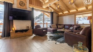 Un salon chaleureux avec une cheminée, des canapés en cuir et une grande fenêtre donnant sur un paysage enneigé.