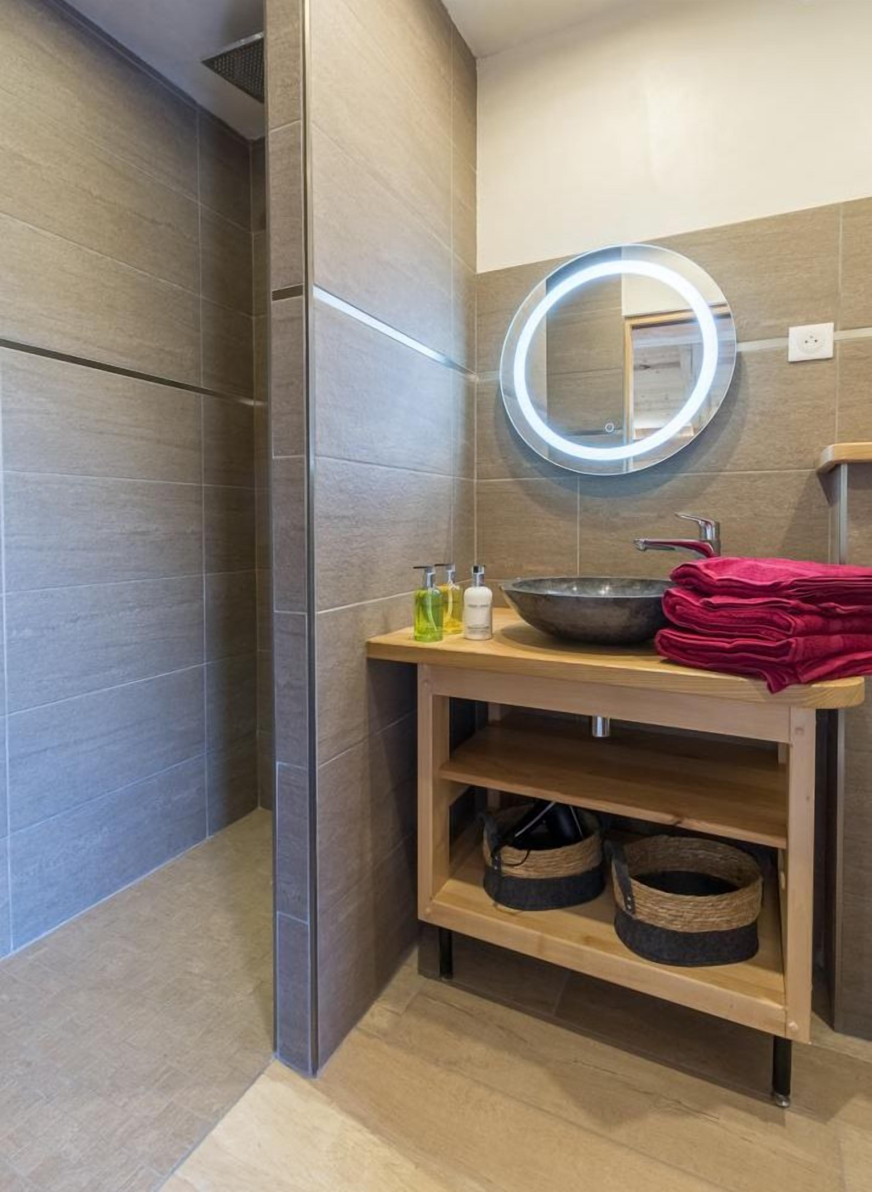 Un baño moderno con un espejo redondo, un lavabo y una repisa con cestas.