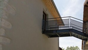 A modern building with a stone facade, a wooden sloped roof, and a metal balcony. - Gite DU Miron - St-paul-sur-yenne (ST-PAUL-SUR-YENNE)