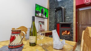 Un coin repas avec une table dressée pour deux personnes, une bouteille de vin, une tasse décorative et un téléviseur diffusant une scène mettant en scène un éléphant.