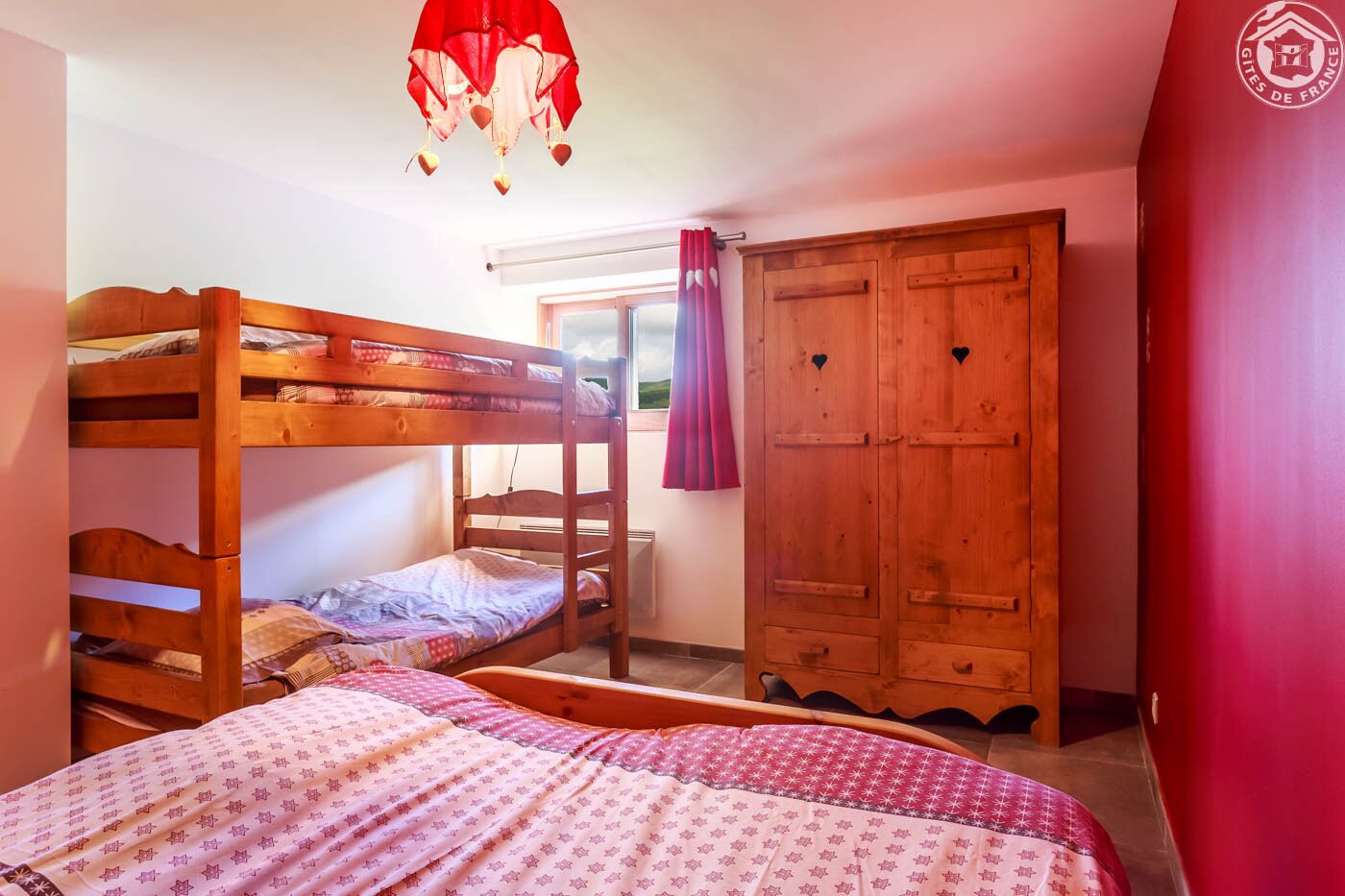 Une chambre avec un lit superposé, une armoire en bois et une fenêtre avec des rideaux.