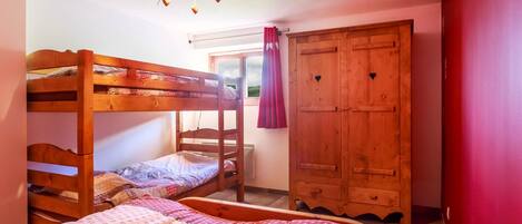 Une chambre avec un lit superposé, une armoire en bois et une fenêtre avec des rideaux.