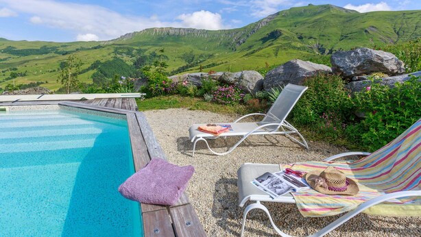 Un espace aménagé au bord de la piscine, avec vue sur des collines verdoyantes, comprenant un fauteuil de relaxation et une petite table sur laquelle sont posés un chapeau et des lunettes de soleil.