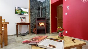 Une pièce chaleureuse avec un mur en pierre, une cheminée, une table en bois sur laquelle repose un magazine, une guitare et un téléviseur fixé au mur.