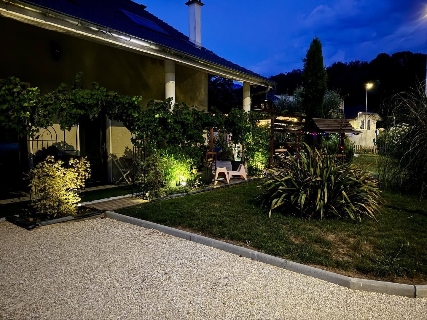 A building with a covered outdoor seating area, a gravel driveway, and various plants.