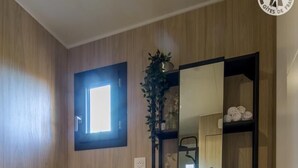 Une salle de bain moderne avec un mur en bois, des toilettes blanches, un lavabo avec un miroir au-dessus et une étagère contenant des articles de toilette.