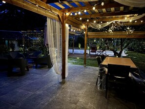 En udendørs patio med et træbeklædt pergola, lyskæder og et spisebord.