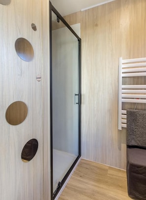 A modern bathroom with a wooden wall, a glass shower enclosure, and a towel rack.