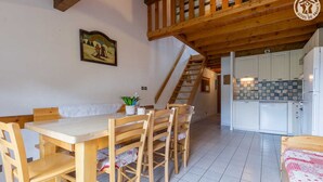 Una habitació acollidora amb una taula de dinar de fusta, cadires, un banc, una escala i una zona de cuina amb armaris blancs i un respatller de rajola.