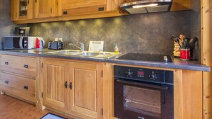 Una cocina compacta con gabinetes de madera, microondas integrado, tostadora y campana extractora de acero inoxidable.