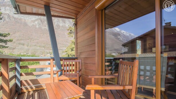 Terraza de madera con dos sillas y una mesa, con vistas a un paisaje montañoso.