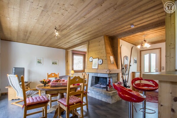 A cozy wooden cabin interior with a dining area, fireplace, and ski equipment.