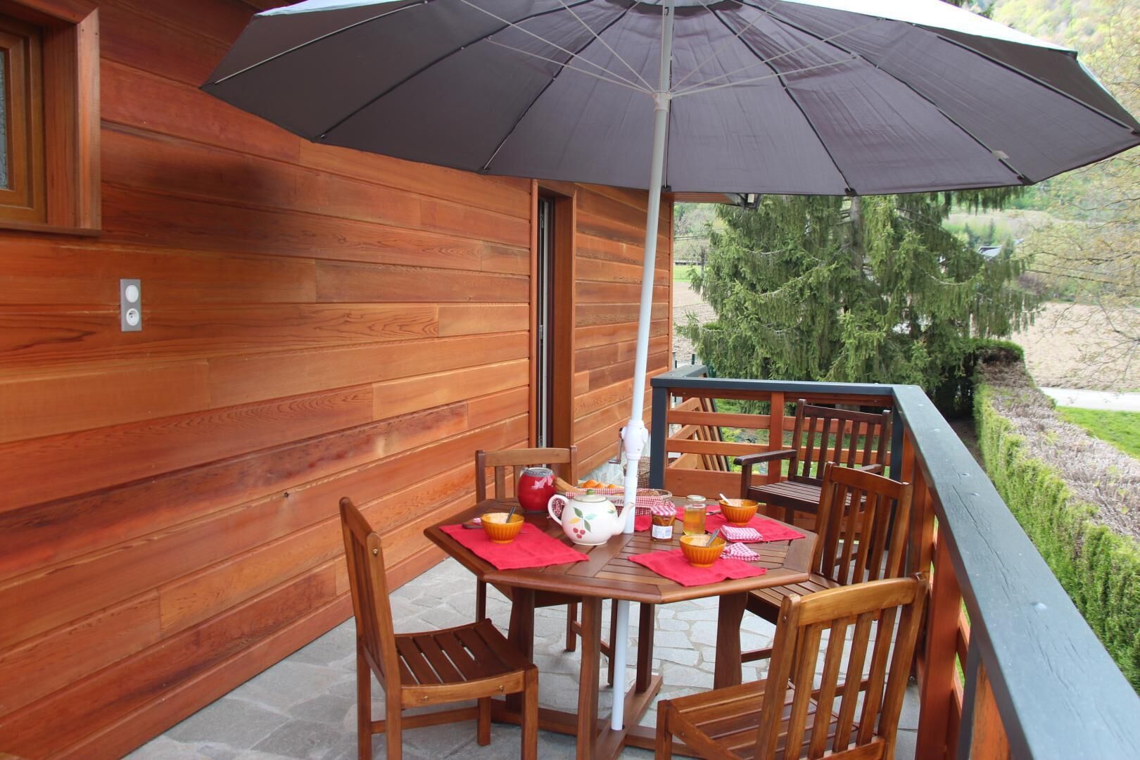 Terraza de madera con mesa y sillas, una sombrilla y vistas a árboles y un estanque.