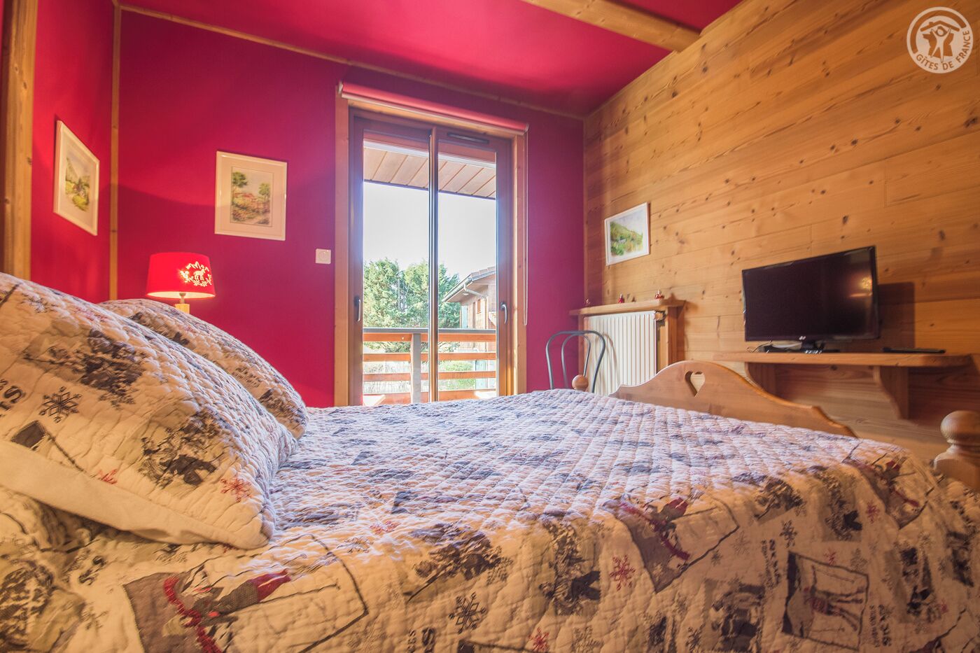 A bedroom with a bed, a television, and a red wall.