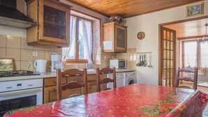 Eine Küche mit Holzschränken, einem Esstisch mit roter Tischdecke, einer Waschmaschine und einer Mikrowelle.