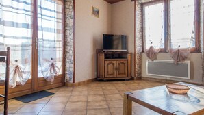 Ein Wohnzimmer mit Fernseher auf einer Holzkommode, einem Esstisch mit Korb und einer Steinwand.