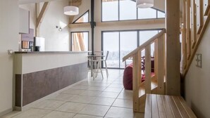Una cocina amplia con encimera de madera y electrodomésticos modernos, un comedor con sillas y banco, y una escalera que conduce a un nivel superior.