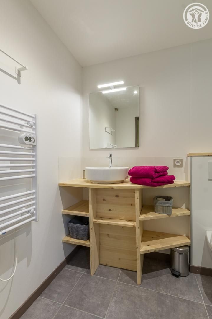 A modern bathroom with a white sink, wooden shelves, a mirror, and a towel rack.