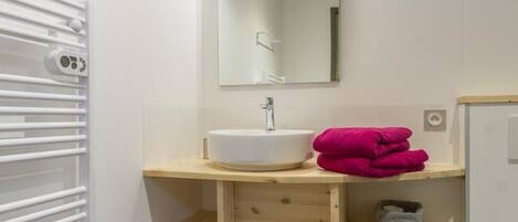A modern bathroom with a white sink, wooden shelves, a mirror, and a towel rack.