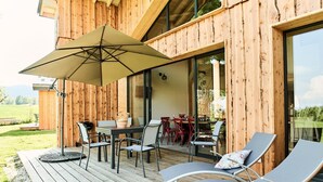 Una terraza de madera con mesa y sillas, un paraguas grande y vista a un comedor.