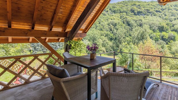 A wooden deck with wicker furniture and a table, overlooking a forested hillside. - L'arveysan - Ste-marie-d'alvey (SAINTE MARIE D'ALVEY)
