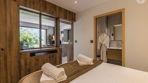 A modern hotel room with a wooden accent wall, a large window, a bed with two white towels, a bathroom with a mirror, and a robe hanging on the door. - L'arveysan - Ste-marie-d'alvey (SAINTE MARIE D'ALVEY)