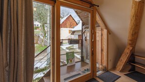 A wooden-framed sliding glass door leading to a balcony with a view of a rustic building and a snowy landscape. - UN Loft A LA Campagne (SAINT JEAN D'ARVEY)
