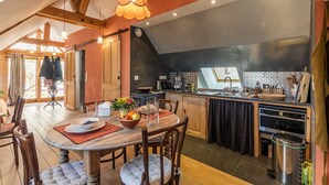 A modern kitchen with a dining area, featuring a wooden table, chairs, and a fruit bowl. - UN Loft A LA Campagne (SAINT JEAN D'ARVEY)