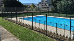 Ein rechteckiger Swimmingpool, umgeben von einem schwarzen Zaun, mit einer Rasenfläche und einem gepflasterten Weg im Vordergrund.
