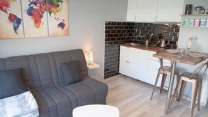 Eine moderne Küche mit schwarzem Fliesenrückwand, weißen Schränken und Edelstahlgeräten. Es gibt einen Essbereich mit einem Holztisch und Metallstühlen.
