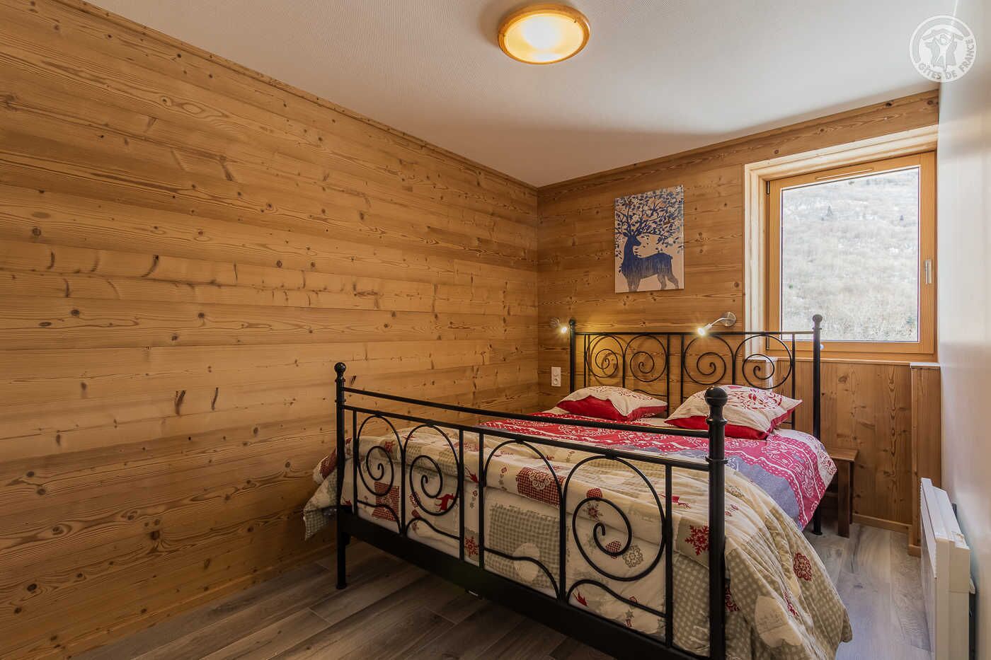 Une pièce aux murs lambrés, avec un lit, une fenêtre et un luminaire au plafond.