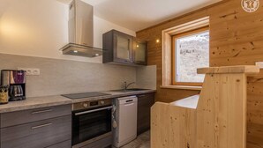 A modern kitchen with a built-in oven, dishwasher, and a window with a view of a snowy landscape. - Gites DE Beaune - LE Brequin (SAINT MICHEL DE MAURIENNE)
